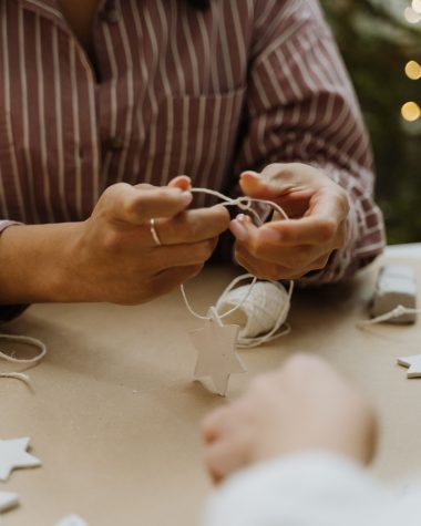 Handen die met touw zelfgemaakte kerststerren in elkaar zetten op een knutseltafel