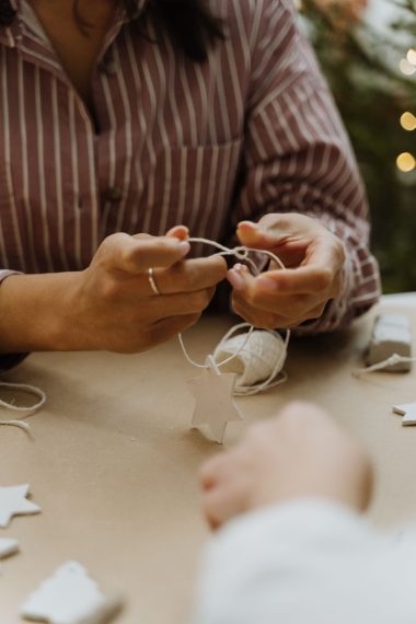 Handen die met touw zelfgemaakte kerststerren in elkaar zetten op een knutseltafel
