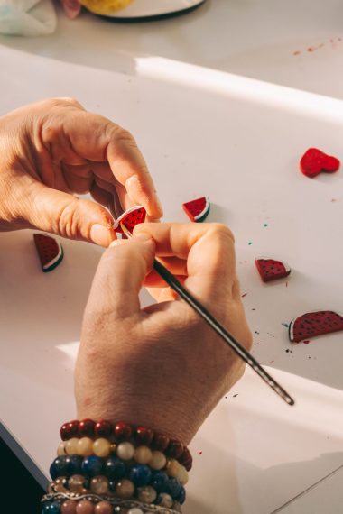 Handen boetseren kleine watermeloentjes van polymeerklei op tafel, een makkelijk beginnersproject voor sieraden