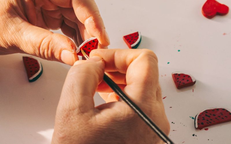 Handen boetseren kleine watermeloentjes van polymeerklei op tafel, een makkelijk beginnersproject voor sieraden
